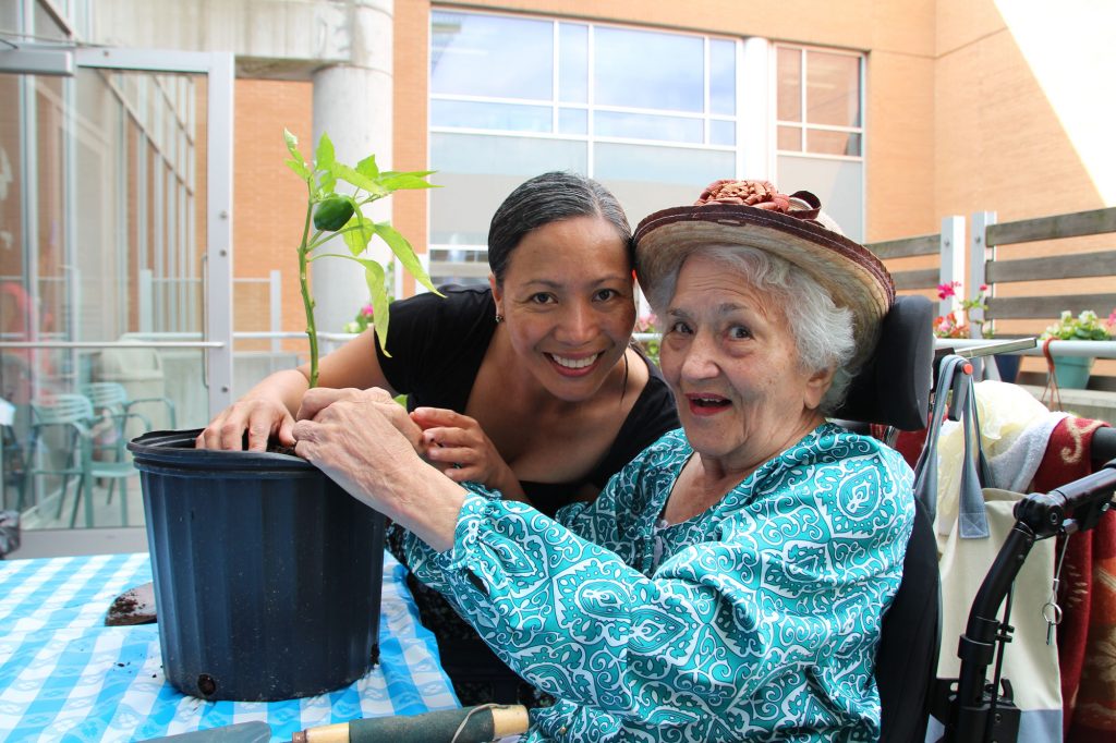 A team members helps a female resident planting a flower into a pot on a table